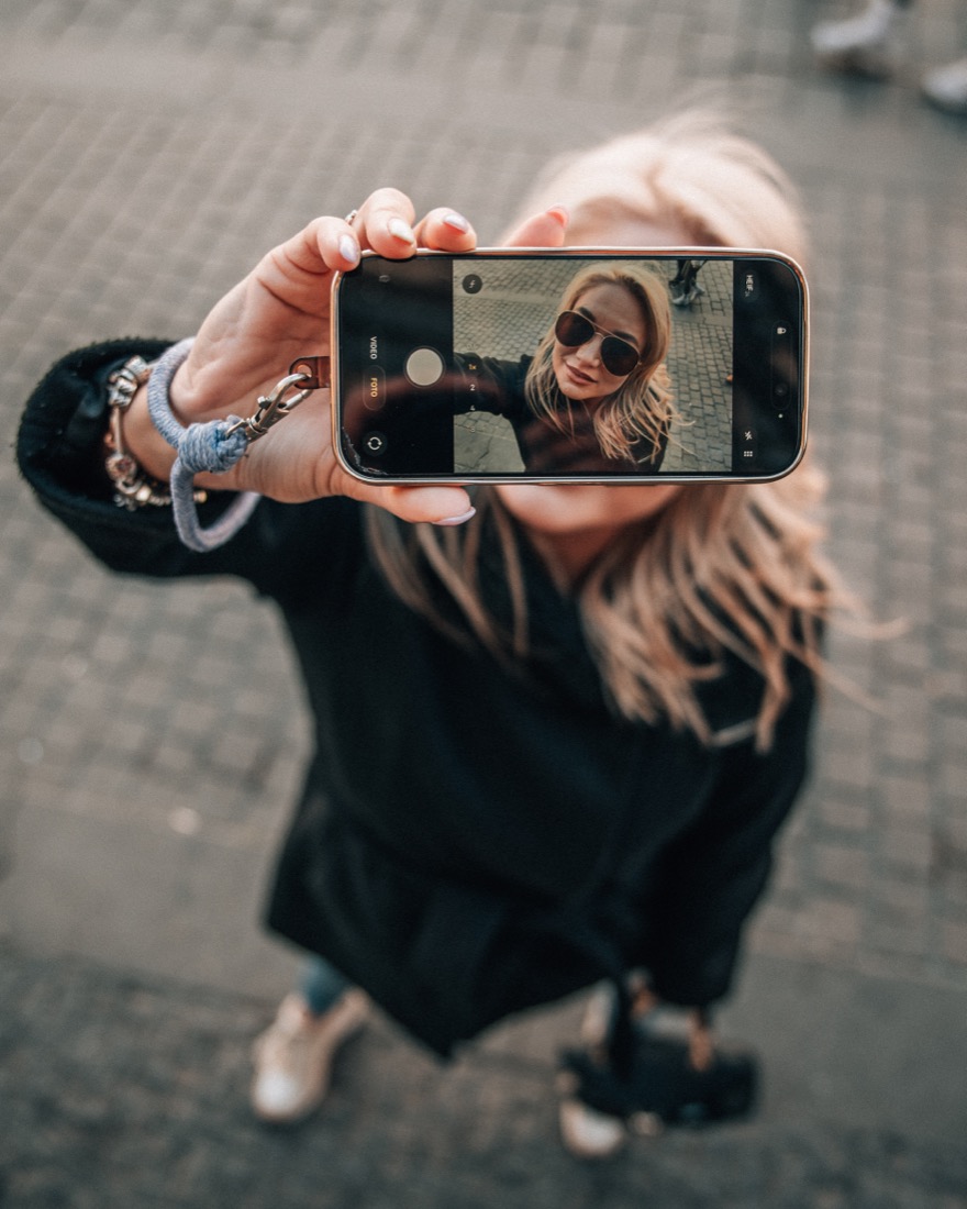 Dívka si fotí selfie na mobil v ulici s dlažebními kostkami