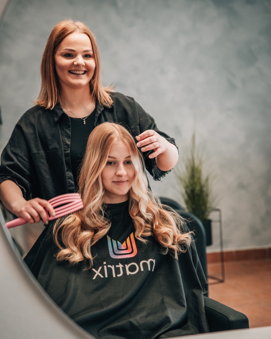 Kadeřnice stylizuje dlouhé vlnité vlasy klientce v zrcadle